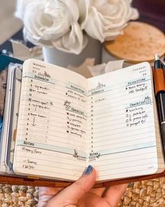 a person holding an open book with writing on it next to a pen and flowers