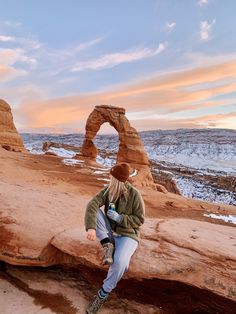 a woman sitting on top of a rock formation in the desert with an arch in the background