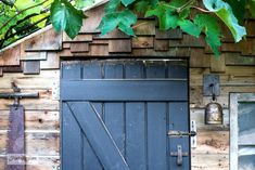 an old wooden building with a black door and green leaves hanging over it's doorway