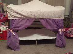 a child's bed with purple curtains and pink toys on the floor next to it