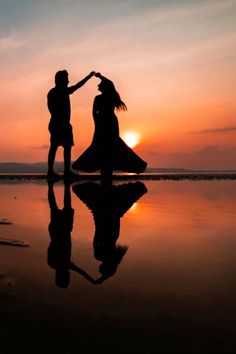 two people are standing on the beach with their arms around each other as the sun sets