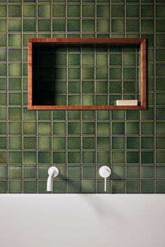 a bathroom with green tiled walls and two white faucets in front of the mirror