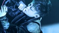 a man with black hair and tattoos on his arm holding a microphone in front of him