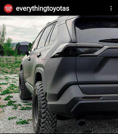 the front end of a gray suv parked on top of a gravel road next to grass and trees