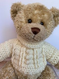 a brown teddy bear wearing a sweater sitting on top of a wooden floor next to a white wall