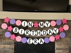 a birthday banner with pink, purple and white stars hanging on a fireplace mantel