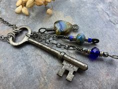 three antique keys are sitting on top of a stone surface with beads and chains hanging from them