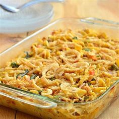 a casserole dish with noodles and vegetables in it on a wooden table next to a spoon