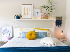 a white bed topped with pillows and blankets next to a shelf filled with potted plants