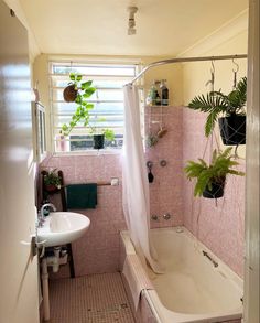 a bath tub sitting next to a white sink under a window in a pink tiled bathroom