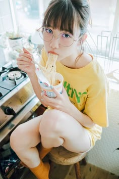 a woman sitting on a chair eating noodles with chopsticks in her hand and looking at the camera