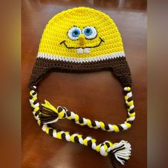 a crocheted yellow and brown hat with blue eyes on top of a wooden table