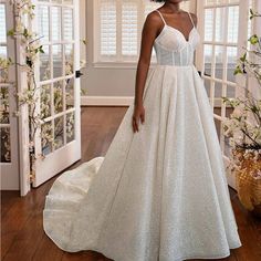 a woman in a white wedding dress standing on a wooden floor with windows behind her