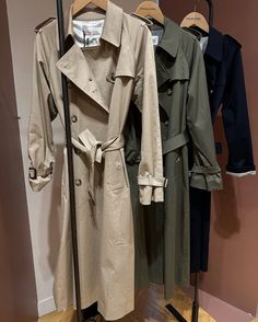 three trench coats hanging on a rack in a clothing store