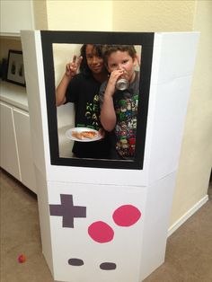 two children are eating and drinking in a video game machine made out of cardboard boxes