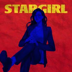 a woman sitting on the ground in front of a red wall with stargirl written on it