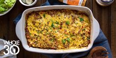 a casserole dish with meat, cheese and vegetables on the table next to it