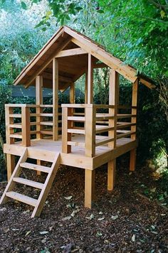 a wooden play house in the woods with stairs leading up to it's roof