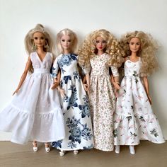 three barbie dolls standing next to each other on a wooden floor in front of a white wall