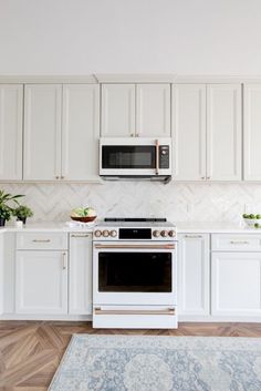 a white kitchen with an oven, microwave and rug on the floor in front of it