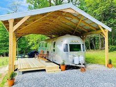 an rv is parked under a carport in the middle of a gravel lot with potted plants