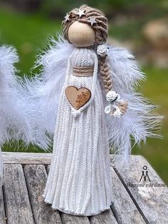 two small white dolls are sitting on a wooden table and one is holding a heart