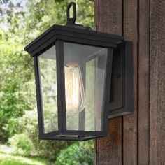 an outdoor light hanging on the side of a wooden building with trees in the background