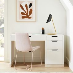 a white desk with a chair, lamp and pictures on the wall above it in a room