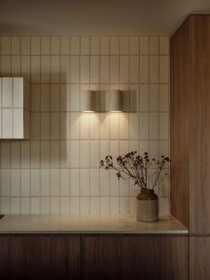 a vase with flowers sitting on top of a counter next to a mirror and light