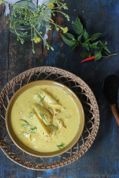 there is a bowl of soup on the table next to some spoons and flowers