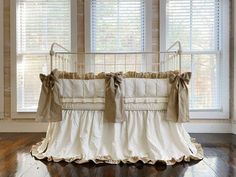 a baby crib in front of two windows with white curtains and brown bows on it