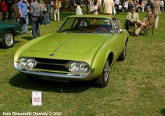 an old green car parked on top of a grass covered field next to other cars