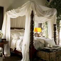 a canopy bed with white drapes and pillows on it's sides, in a bedroom