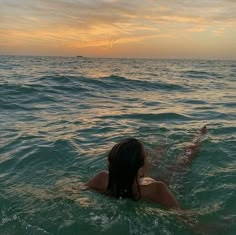 a woman swimming in the ocean at sunset