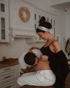 a man and woman hug while sitting on a counter in a kitchen with white cabinets