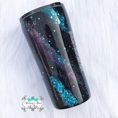 the black and blue glitter tumbler is sitting on a white fur covered surface,