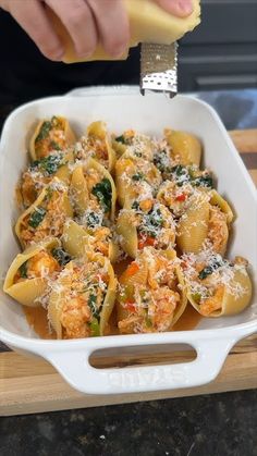 a person is scooping some food out of a casserole dish with cheese and spinach