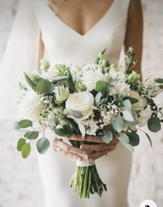 a bride holding a bouquet of white flowers and greenery