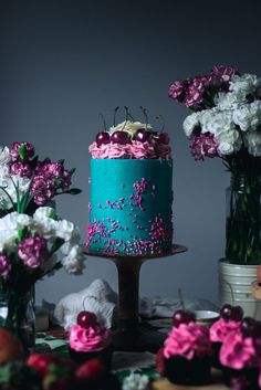 there is a blue cake with pink sprinkles and flowers in vases