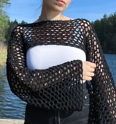 a woman is standing by the water wearing a black crochet sweater