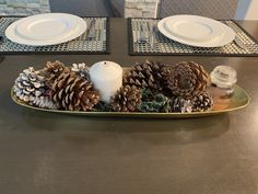 pine cones and candles sit on a gold tray with white plates in the back ground