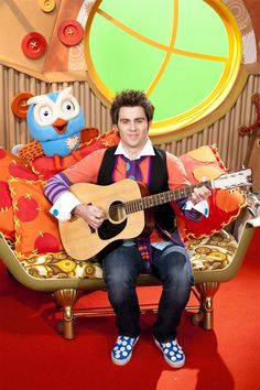 a man sitting on top of a couch holding a guitar in front of an owl