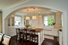 a large kitchen with white cabinets and wooden table surrounded by stools in front of an island