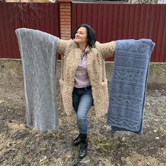 a woman holding up two blankets in front of a red brick building with a fence behind her