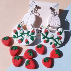 the earrings are decorated with strawberries and leaves on white buttons, along with two smaller red strawberrys