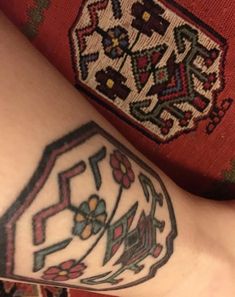 a close up of a person's arm with tattoos on it and an embroidered object in the background