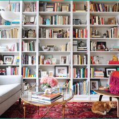 a living room filled with lots of books on top of a white book shelf next to a couch