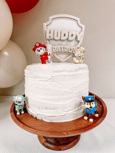 a birthday cake on a wooden stand with balloons in the background