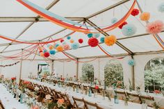 a large tent with tables and chairs covered in paper pom - poms hanging from the ceiling