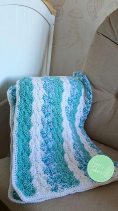 a blue and white crocheted blanket sitting on top of a chair next to a pillow